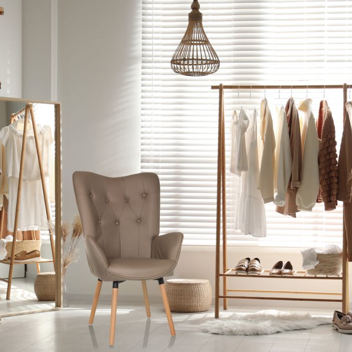 Ein brauner Ohrensessel mit einer Steppung an der Rückenlehne steht in einem modernen Ankleidezimmer in beige-Tönen.